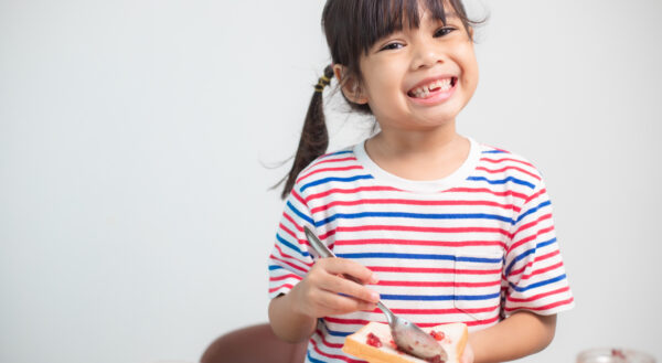 Photo of little girl smiling at the camera making a PB&J sandwich